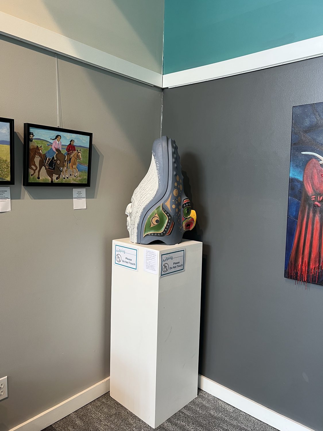Corner of the gallery with paintings and a carved sculpture