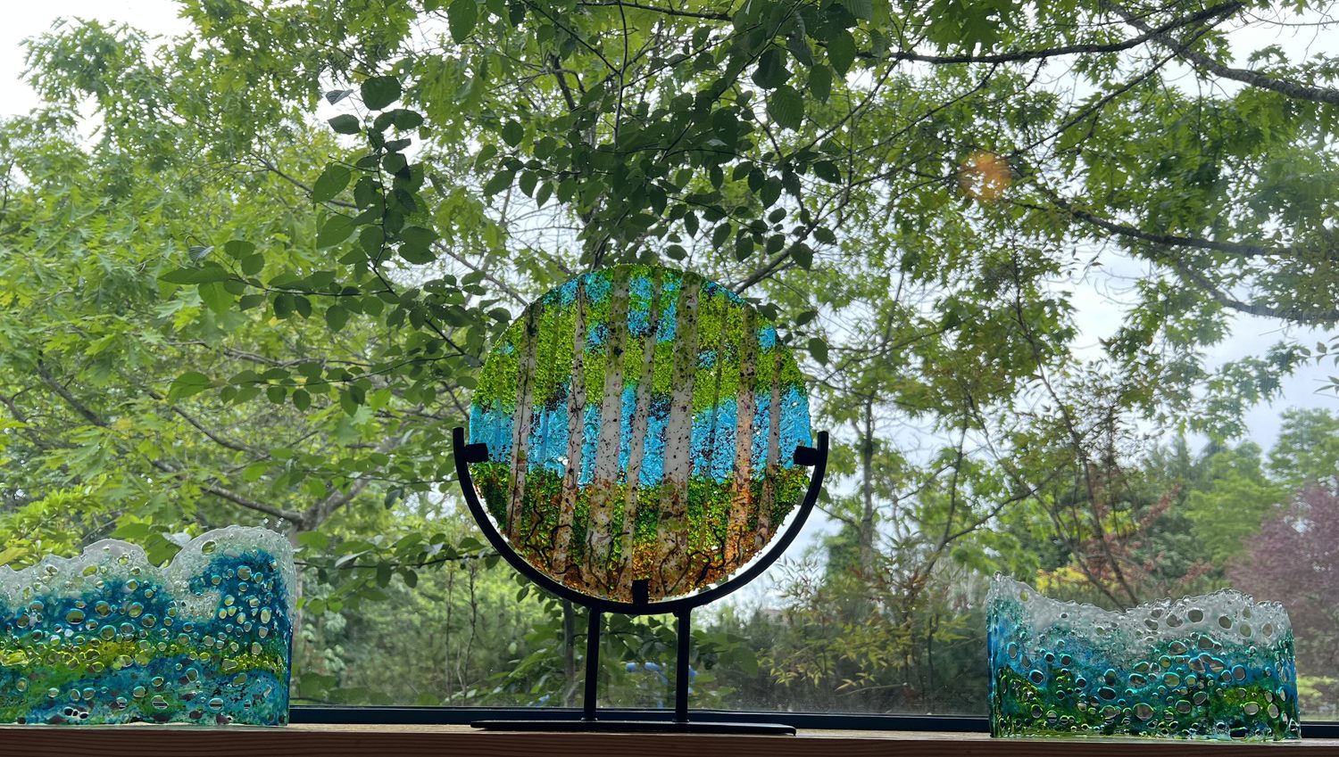 A round fused-glass panel of a birch forest on a stand