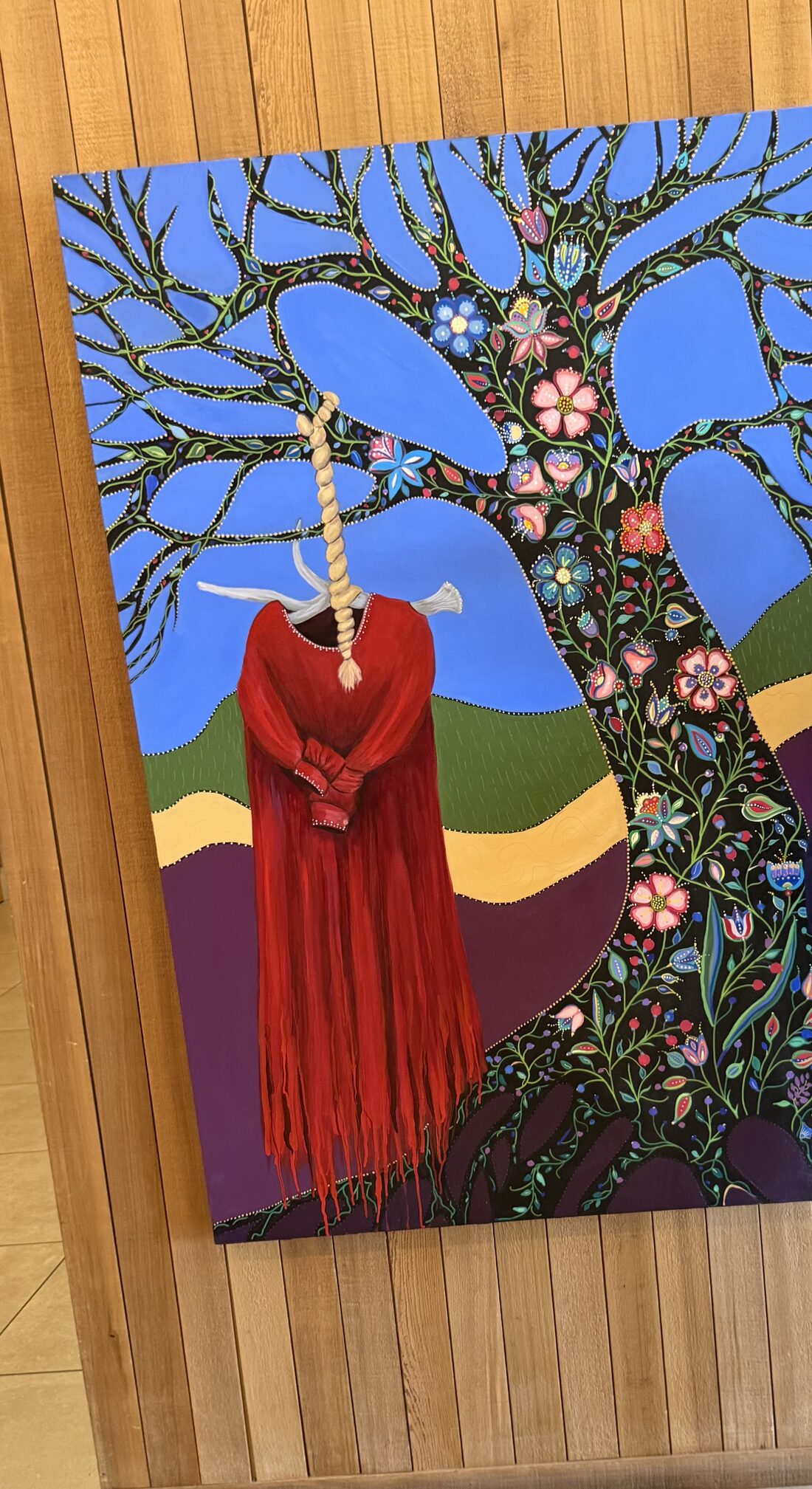 Painting of a red fringed dress hanging from a tree covered in vibrant beaded flowers against a blue sky