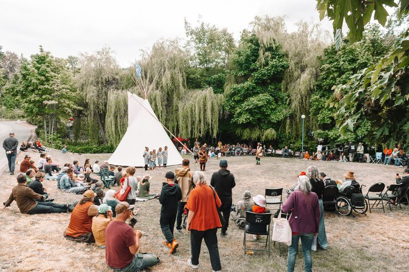Two Knowledge Keepers in cedar hats drumming in front of the tipi