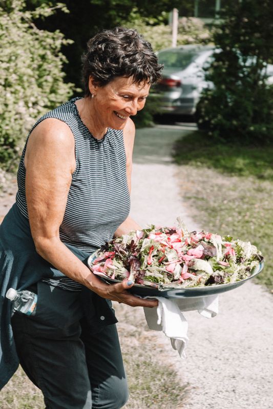 A volunteer carries a large bowl of salad with fresh greens and pink petals to the feast