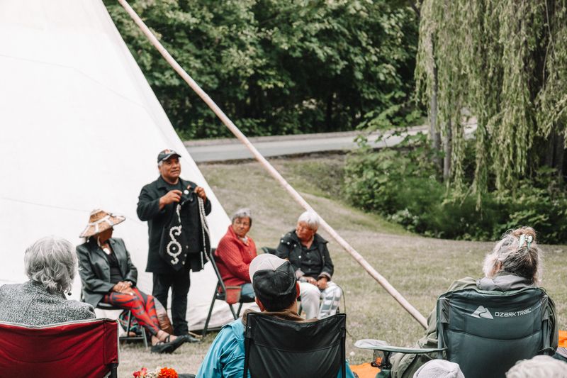 A circle of Elders and community members sitting and visiting under the trees