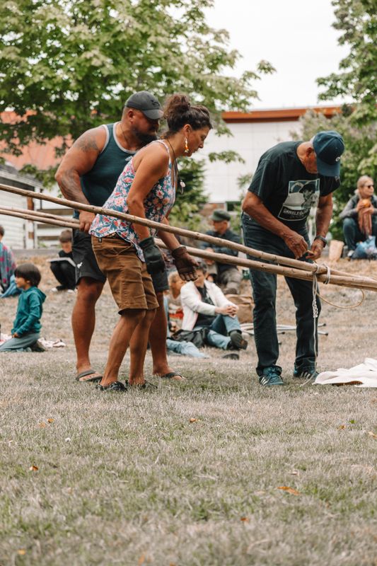 A close view of hands tying lodgepoles together with rope at the tipi raising