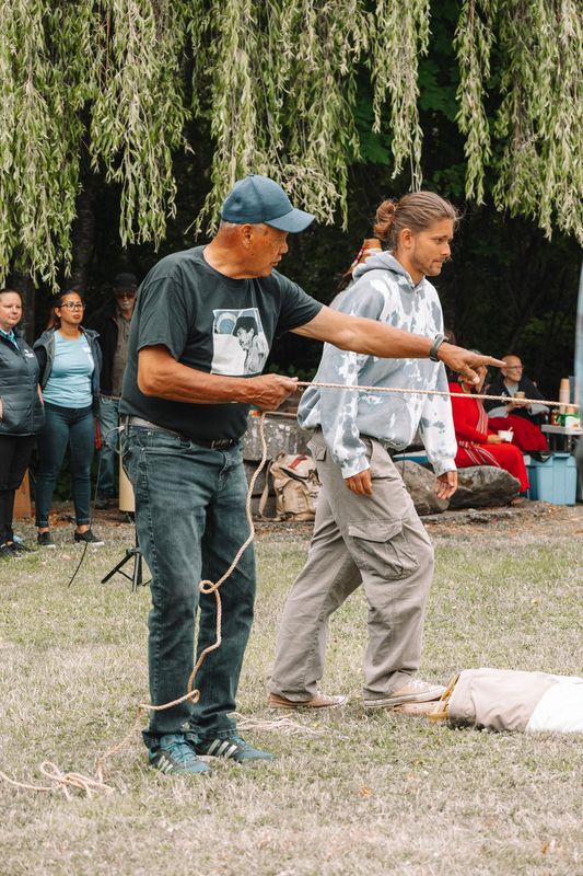Volunteers raise the tipi canvas with the lodgepoles together at the opening of IPW 2025