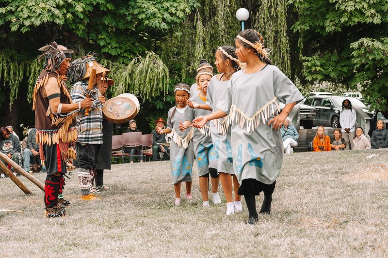 Two dancers in regalia at the tipi, surrounded by community members