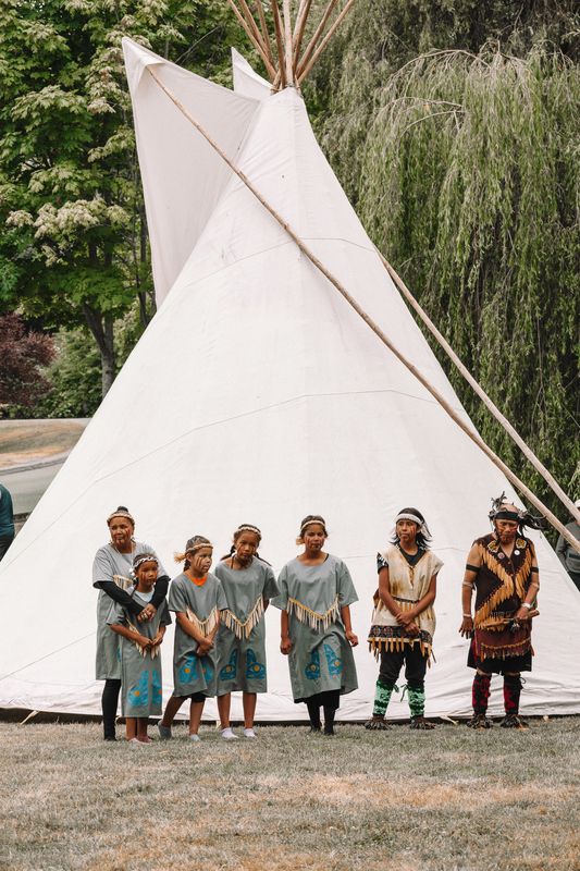 A line of dancers approaches drummers led by an Elder in regalia