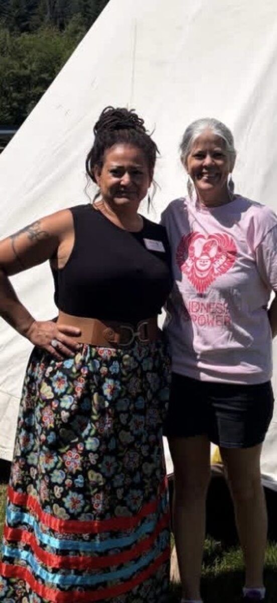 Two women standing together in front of a white tipi at the gathering