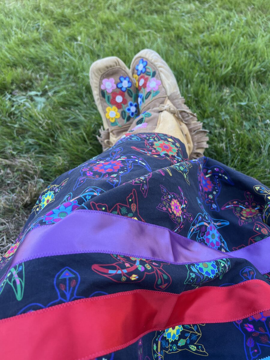 Hand-beaded mukluks with floral beadwork, worn with a printed ribbon skirt, on the grass